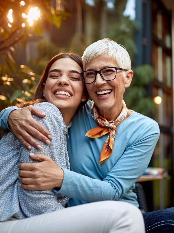 A woman caregiver laughs while hugging and cheerful elderly woman.